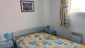 Un dormitori amb un llit, una taula de nit, una làmpada, una finestra amb cortines i una fotografia penjada a la paret.