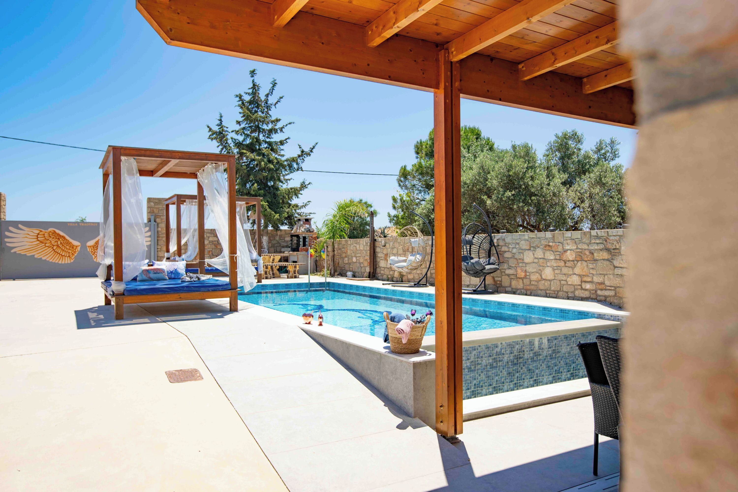 A pool area with a wooden pergola, a stone wall, and a lounge chair.