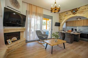 A modern living room with a fireplace, a television, a dining area with a table and chairs, and a kitchen with an archway. - Traounou Serenity Villa (Rhodes)