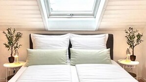 Una camera da letto con un lucernario, un letto con lenzuola bianche, due comodini con lampade e piante in vaso.