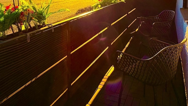 Un balcone con vista su un campo e un tramonto. Sono presenti sedie in vimini e un tavolino.