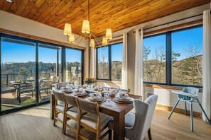 A dining area with a wooden table set for a meal, large windows offering a view of the outdoors, and a wooden ceiling. - Indoor Pool Cabin w/ Views, Hot Tub & Game Room (Sevierville)
