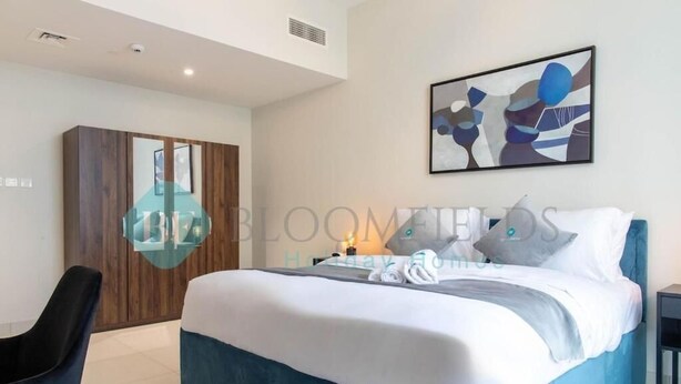 A modern hotel room with a large bed, a wardrobe, and a painting on the wall. - Bloomfields Elegant 1BR in Reflectio (Abu Dhabi)