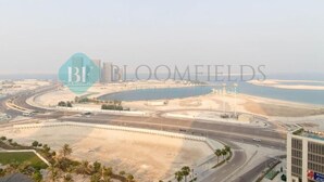 A view of a coastal area with a road curving around a body of water, a large building, and a clear sky. - Bloomfields Elegant 1BR in Reflectio (Abu Dhabi)