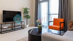 A modern living room with a TV, a round coffee table, a sofa, and an orange chair. - Bloomfields Elegant 1BR in Reflectio (Abu Dhabi)