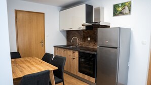 A compact kitchen with a wooden dining table, dark chairs, a stainless steel refrigerator, and a built-in oven. - Charming family apartment with terrace, herb garden views and animals (Štore)