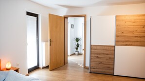 A bedroom with a bed, a nightstand with a lamp, a wooden wardrobe, and a door leading to another room. - Charming family apartment with terrace, herb garden views and animals (Štore)