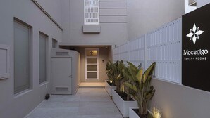 Ein modernes Gebäude mit geschlossenem Eingangsbereich, einem Schild für 'Mocenigo Luxury Rooms' und einem mit Pflanzkübeln gesäumten Weg.