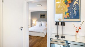 A hotel room with a bed, bedside lamps, a framed abstract artwork, and a vase with flowers. - Aachen South Holiday Apartment for 4 Guests (55 m²) (Aachen)