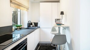 A narrow kitchen with a black countertop, white cabinets, a black stove, and a small chair. - Aachen South Holiday Apartment for 4 Guests (55 m²) (Aachen)