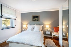 A bedroom with a bed, bedside tables, a chair, a painting, and a window with blinds.
