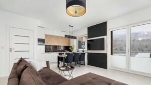 Ein modernes Wohnzimmer mit einer großen braunen Couch, einem Essbereich mit Tisch und Stühlen sowie einer Küche im Hintergrund.