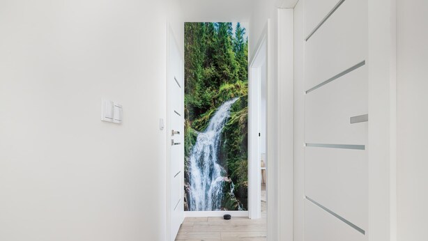 Ein Flur mit Blick auf einen Wasserfall durch eine Tür, Holzboden und weißen Wänden.