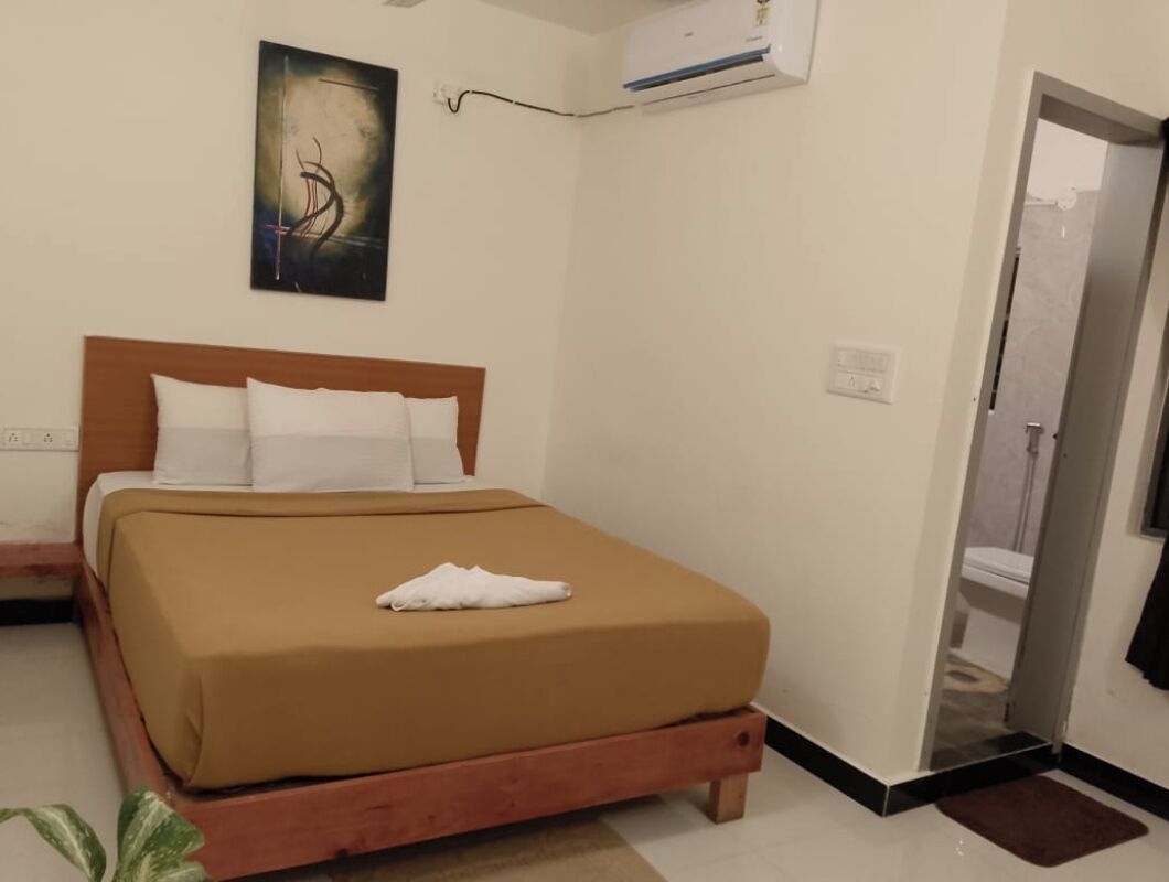 Een slaapkamer met een bed, een schilderij, een airconditioner en een deur naar een badkamer.