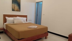 A neatly made bed with a wooden headboard, a single pillow, and a folded blanket on the floor. - Hangout at  Nandi Hills (Devanahalli)