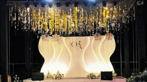 A stage with a white backdrop and the letters "O" and "A" in the center, surrounded by greenery and outdoor seating. - Hangout at  Nandi Hills (Devanahalli)