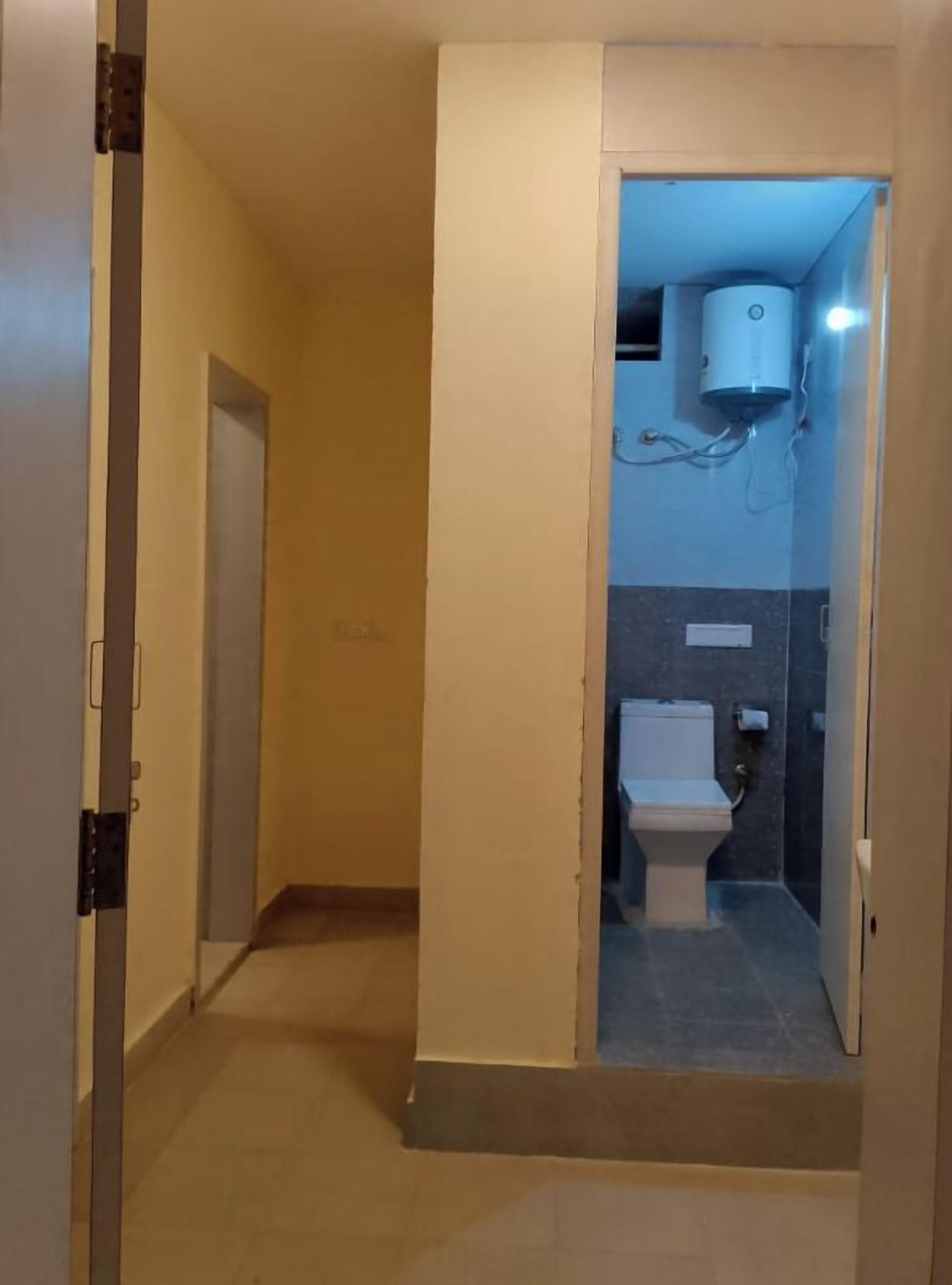 A narrow hallway leading to a bathroom with a toilet, a towel rack, and a wall-mounted air conditioner.