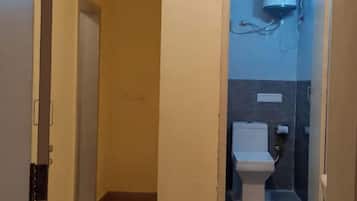 A narrow hallway leading to a bathroom with a toilet, a towel rack, and a wall-mounted air conditioner.
