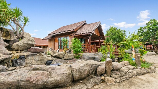 A wooden house with a tiled roof, surrounded by large rocks and various plants. - Chanta Boutique Place (Ubon Ratchathani)
