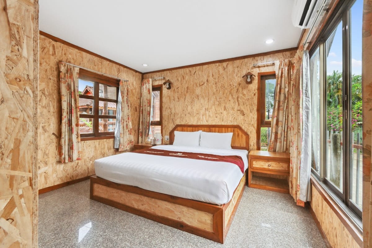 A wooden-paneled room with a large bed, a small bedside table, and a window with curtains.