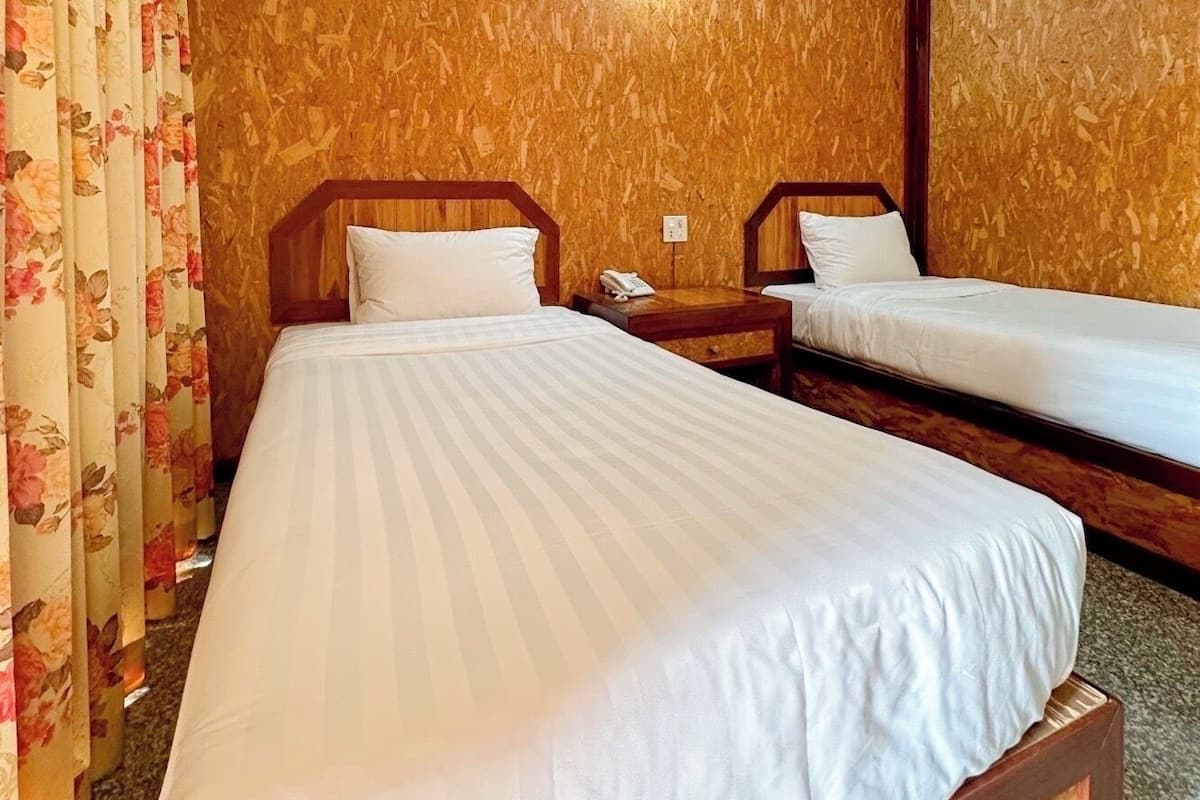 A hotel room with two single beds, wooden headboards, and a floral curtain.