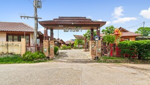 A street entrance with a wooden archway, houses on either side, and a small shrine with a yellow roof. - Chanta Boutique Place (Ubon Ratchathani)