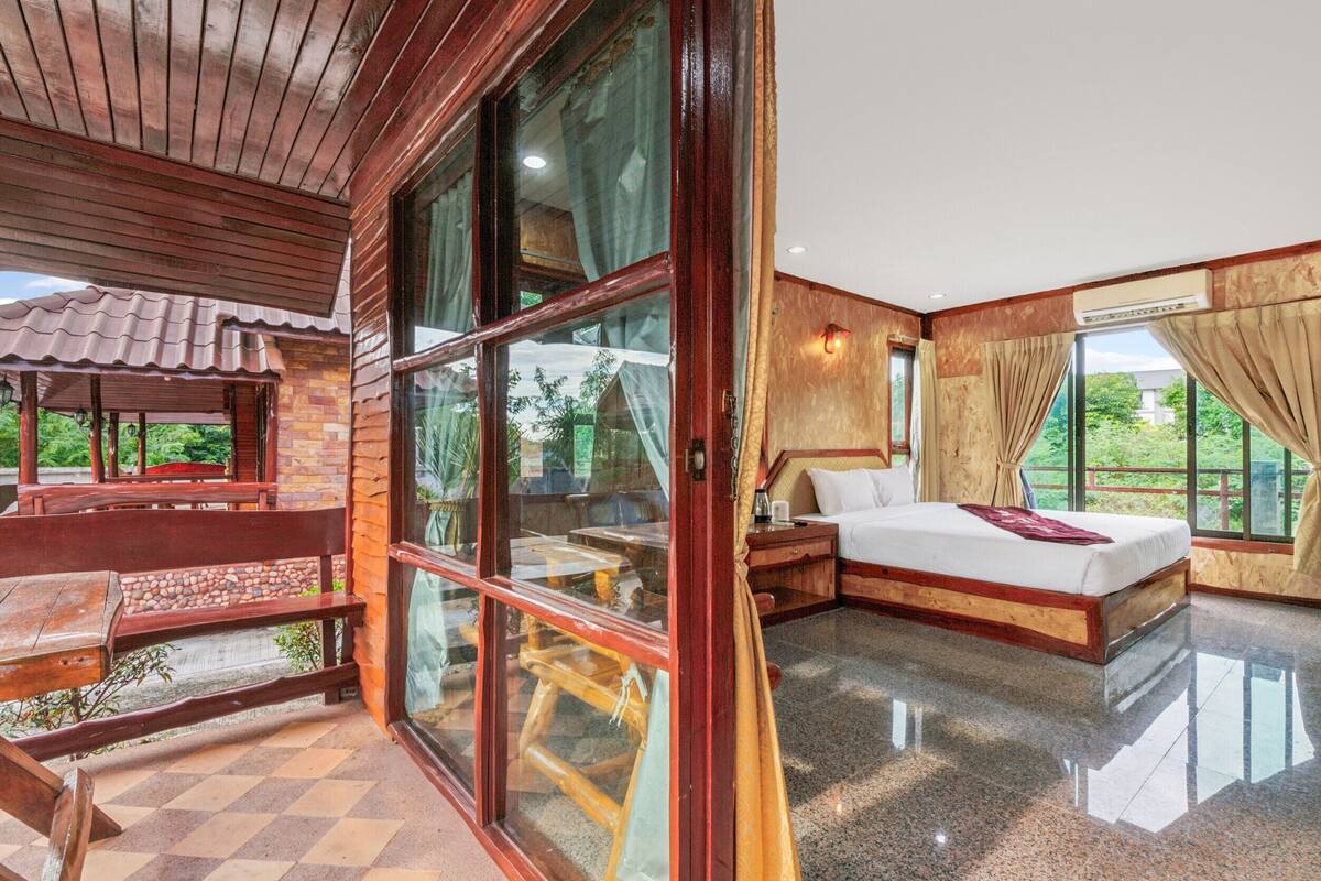 A room with a large bed, a wooden bench, and a view of greenery outside.