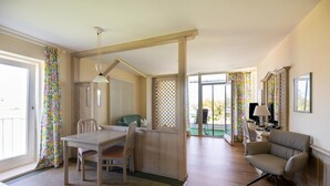 Ein Zimmer mit Esstisch, Stühlen, einer Couch, einem Fernseher und einem Fenster mit Vorhängen.