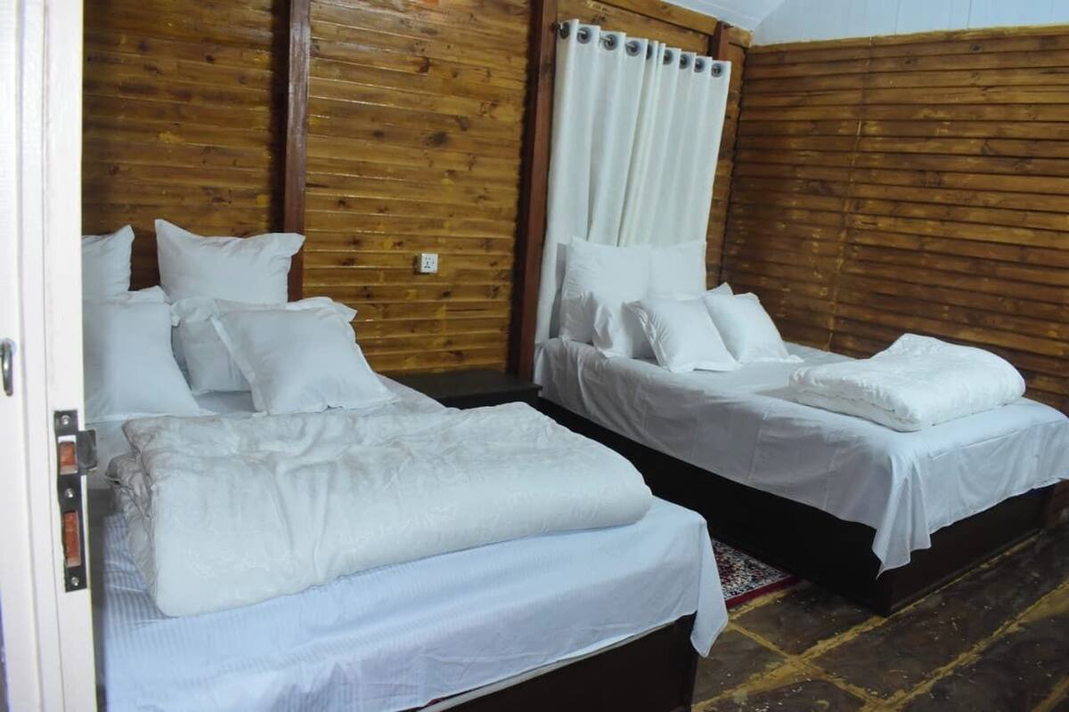 Une chambre avec deux lits, des murs en bois et un rideau.