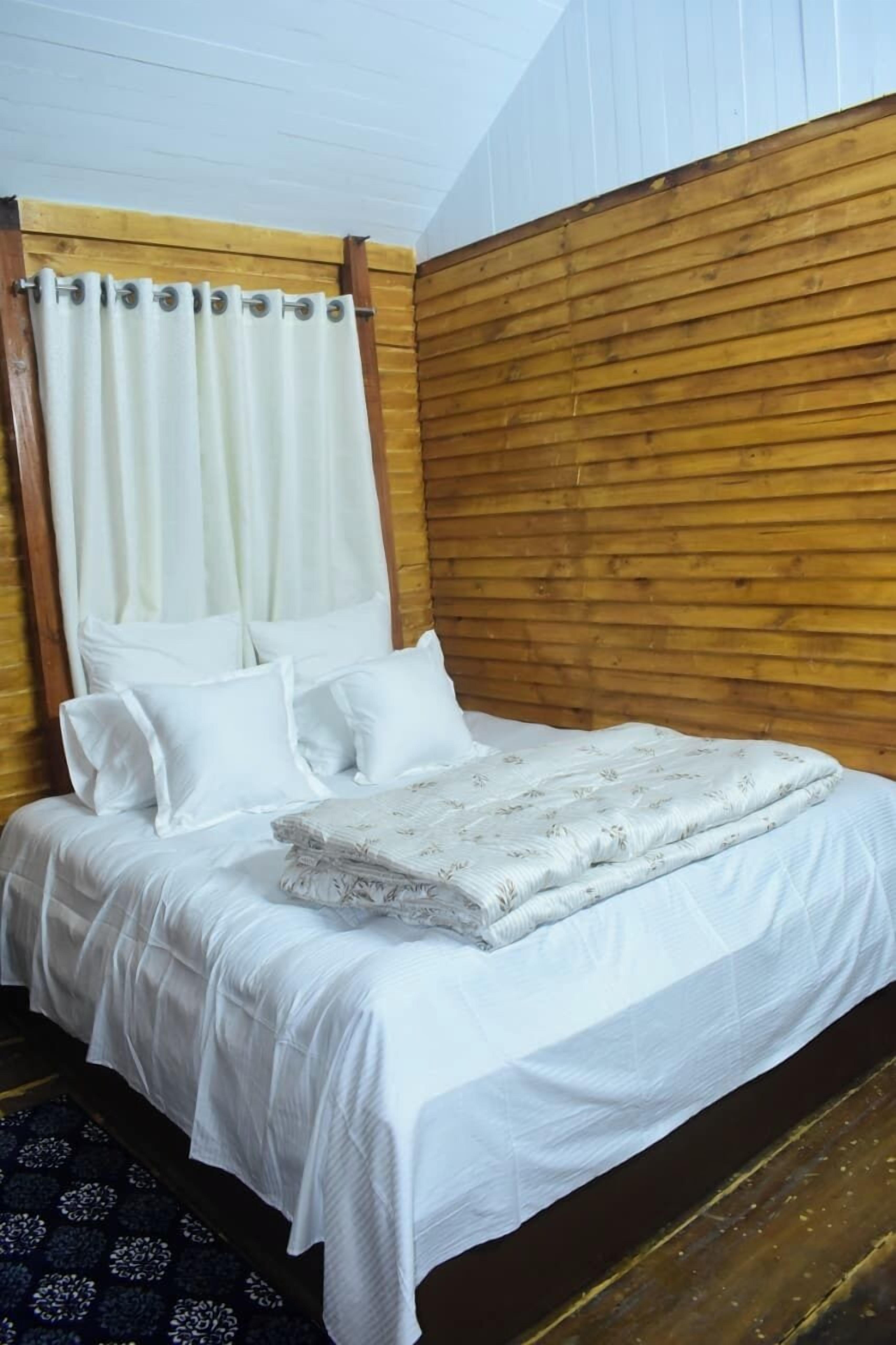A bed with white bedding, a floral-patterned blanket, and a wooden headboard.
