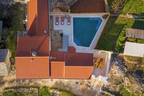 Oversigtsbillede af en ejendom med swimmingpool, overdækket terrasse og en bygning med rødt tag.