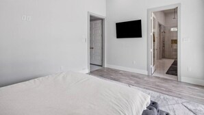 A modern bedroom with a bed, a ceiling fan, and a flat-screen TV mounted on the wall. - One Story + Generator & Gated Near HTX Medical (Houston)