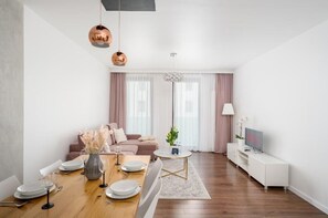 A modern living room with a dining area, a sofa, a TV, and a lamp. - Malila Premium Apartments Cystersów 20D (Kraków)