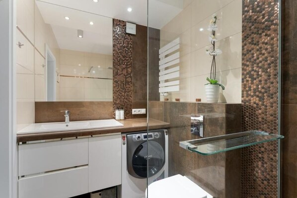 A modern bathroom with a large mirror, a sink, a washing machine, and a glass shelf. - Malila Premium Apartments Cystersów 20D (Kraków)