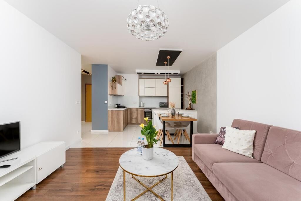 A modern living room with a flat-screen TV, a round coffee table, and a pink sofa.
