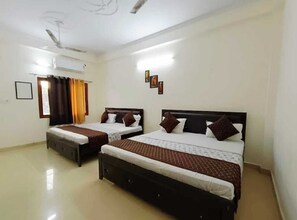 A hotel room with two single beds, a ceiling fan, an air conditioning unit, and a window with curtains. - AYODHYA, the oldest and most divien citi for Hindu in India. Come & Explore RAM. (Q6J4+PX Ayodhya, Uttar Pradesh)