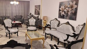 A living room with a grey sofa set, a glass coffee table, and a chandelier. - Spacious 3-Bedroom Apartment in Central Cairo with City View (Cairo Governorate)
