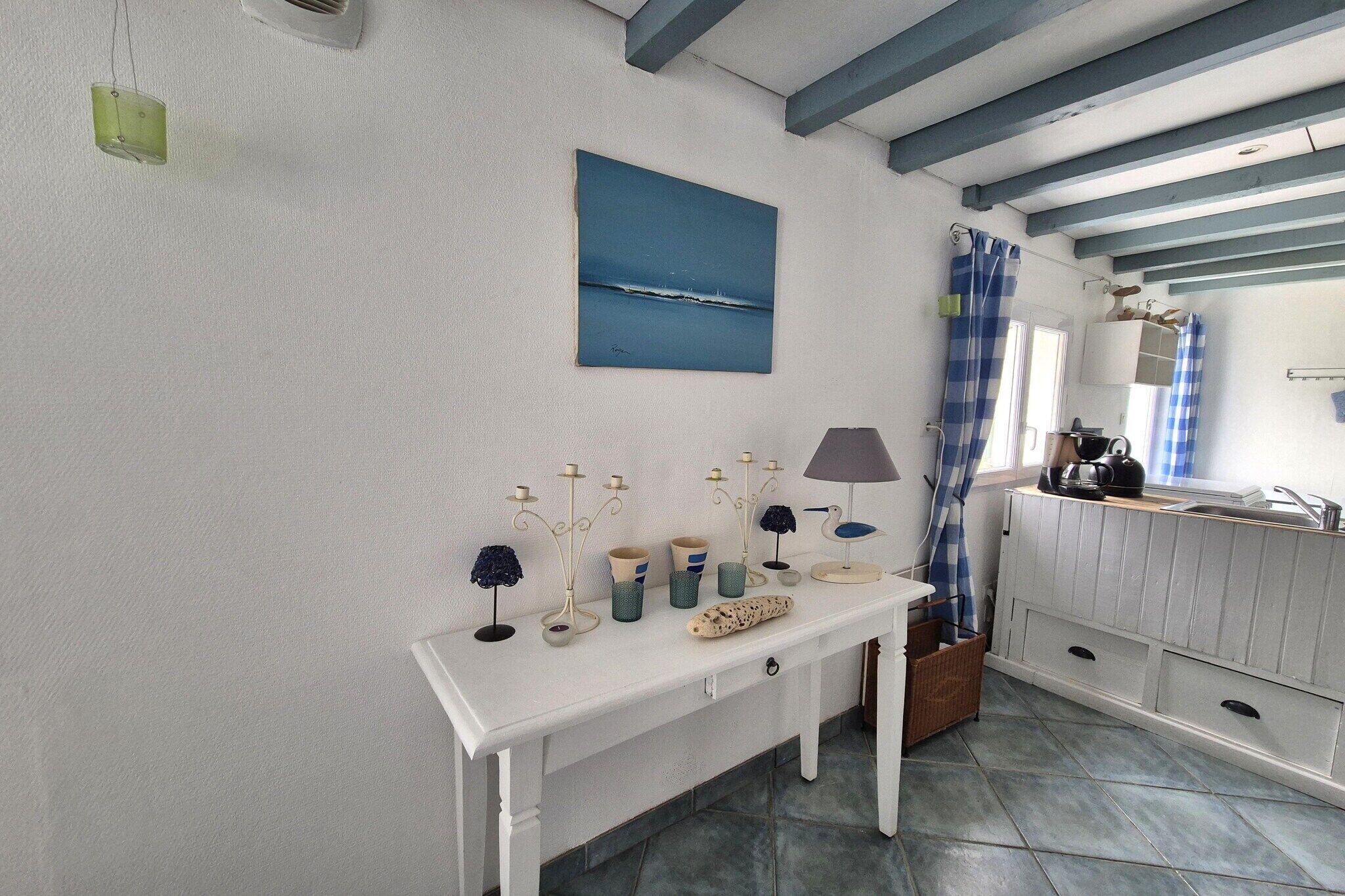 A white table with decorative items, a blue painting, and a kitchen area with a sink and cabinets.