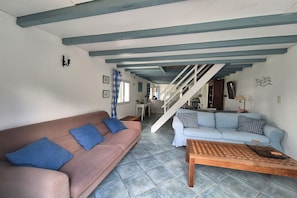 Ein Wohnzimmer mit braunem Sofa, blauen Kissen, einem hellblauen Sofa, einem Holztisch und einer Treppe, die in einen anderen Raum führt.