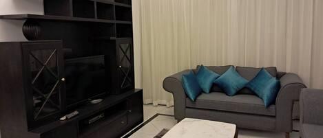 A living room with a dark entertainment unit, a grey sofa with blue cushions, and a white marble coffee table.