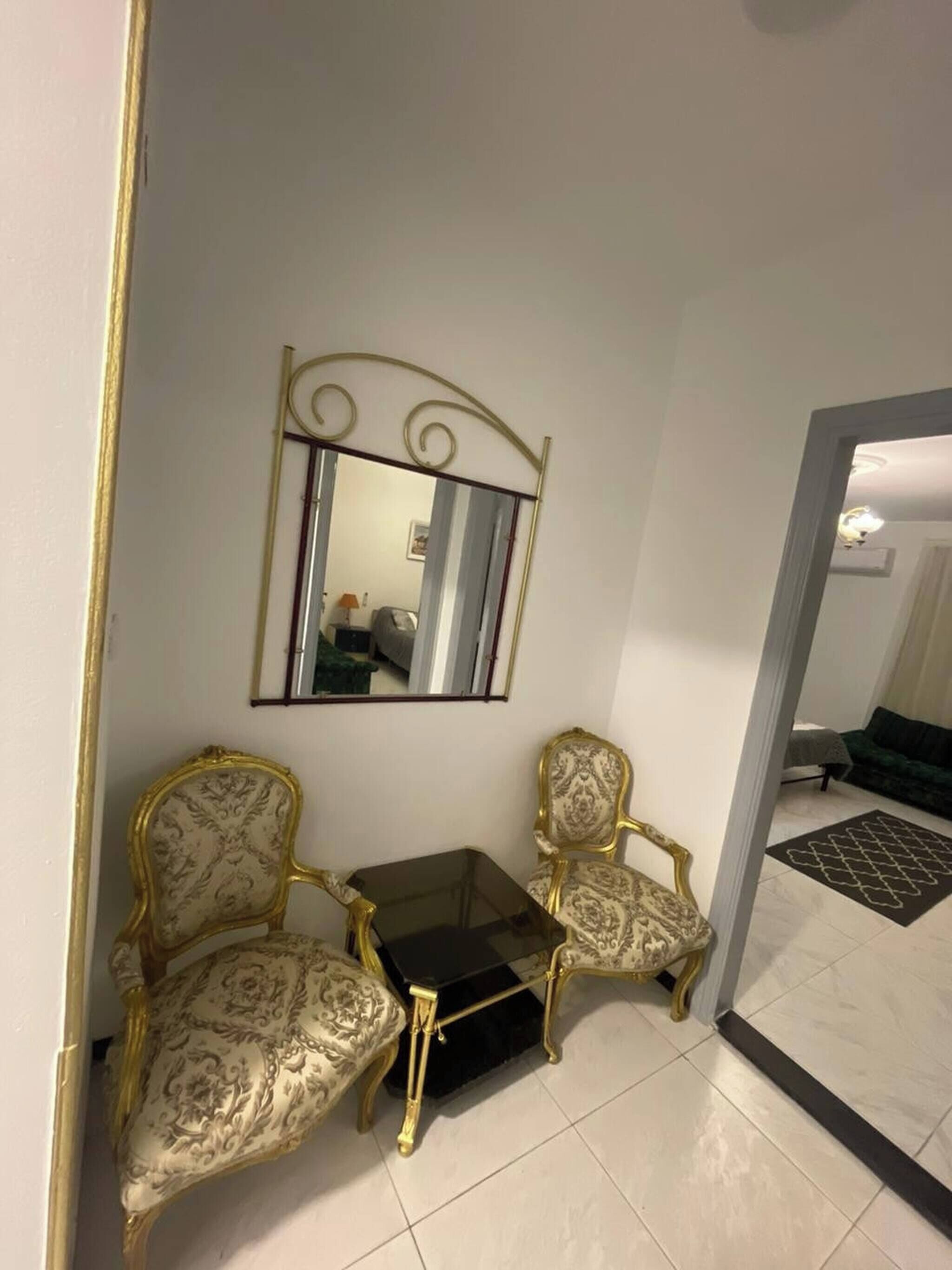 Une pièce comprenant deux fauteuils richement décorés, une petite table et un miroir fixé au mur.