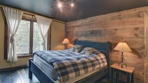 A bedroom with a wooden headboard, a bed with plaid bedding, two bedside lamps, and a window with curtains.