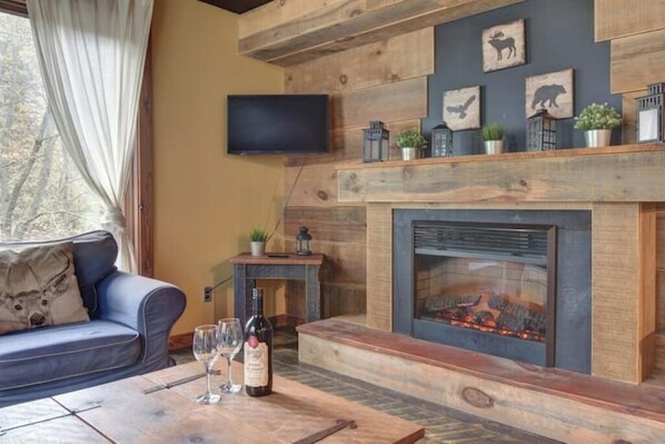 Una sala de estar acogedora con chimenea, un sofá y una mesa de centro con copas de vino y una botella.