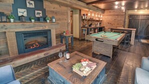 A cozy indoor space with a pool table, a fireplace, and a dining area with a wooden table set for a meal.