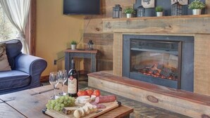 A cozy living room with a fireplace, a wooden coffee table with a cheese board, and a blue sofa.