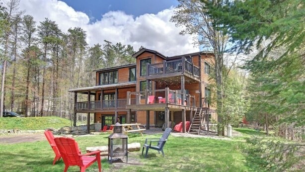 A two-story cabin with a balcony, surrounded by a forest.