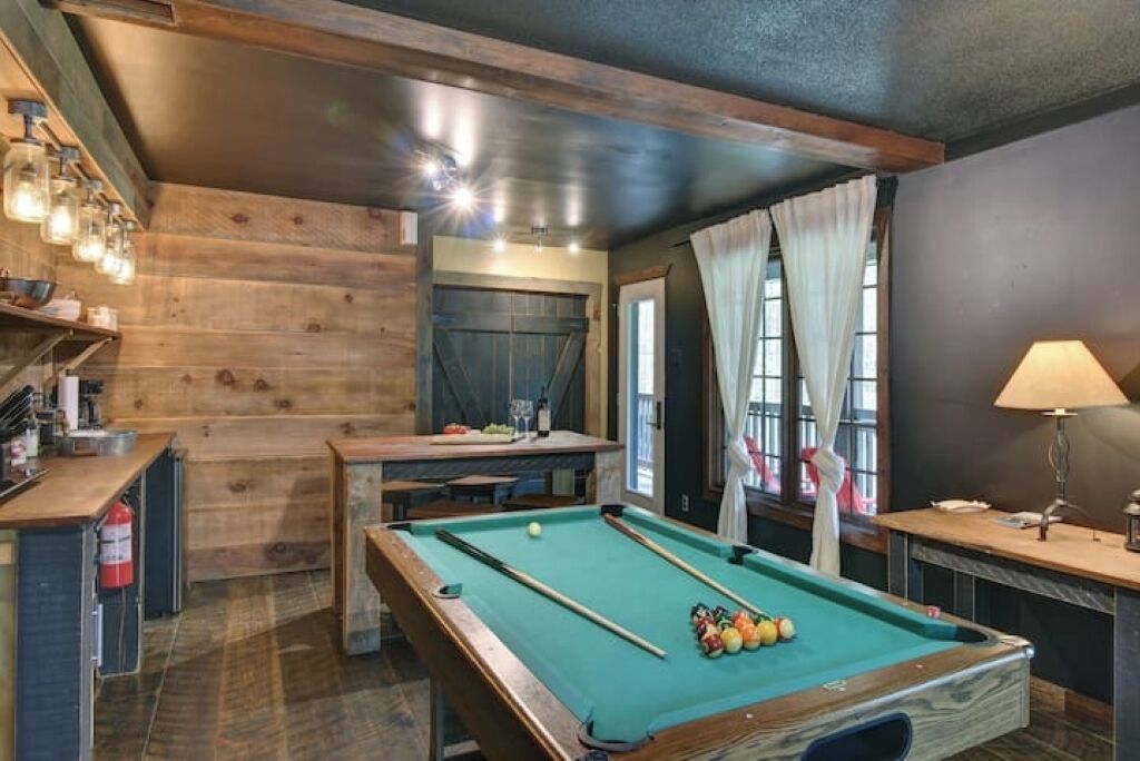 Une table de billard dans une pièce aux murs en bois et dotée d’un luminaire au plafond.