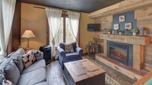 A cozy living room with a fireplace, a sofa, a coffee table, and a television mounted on the wall.