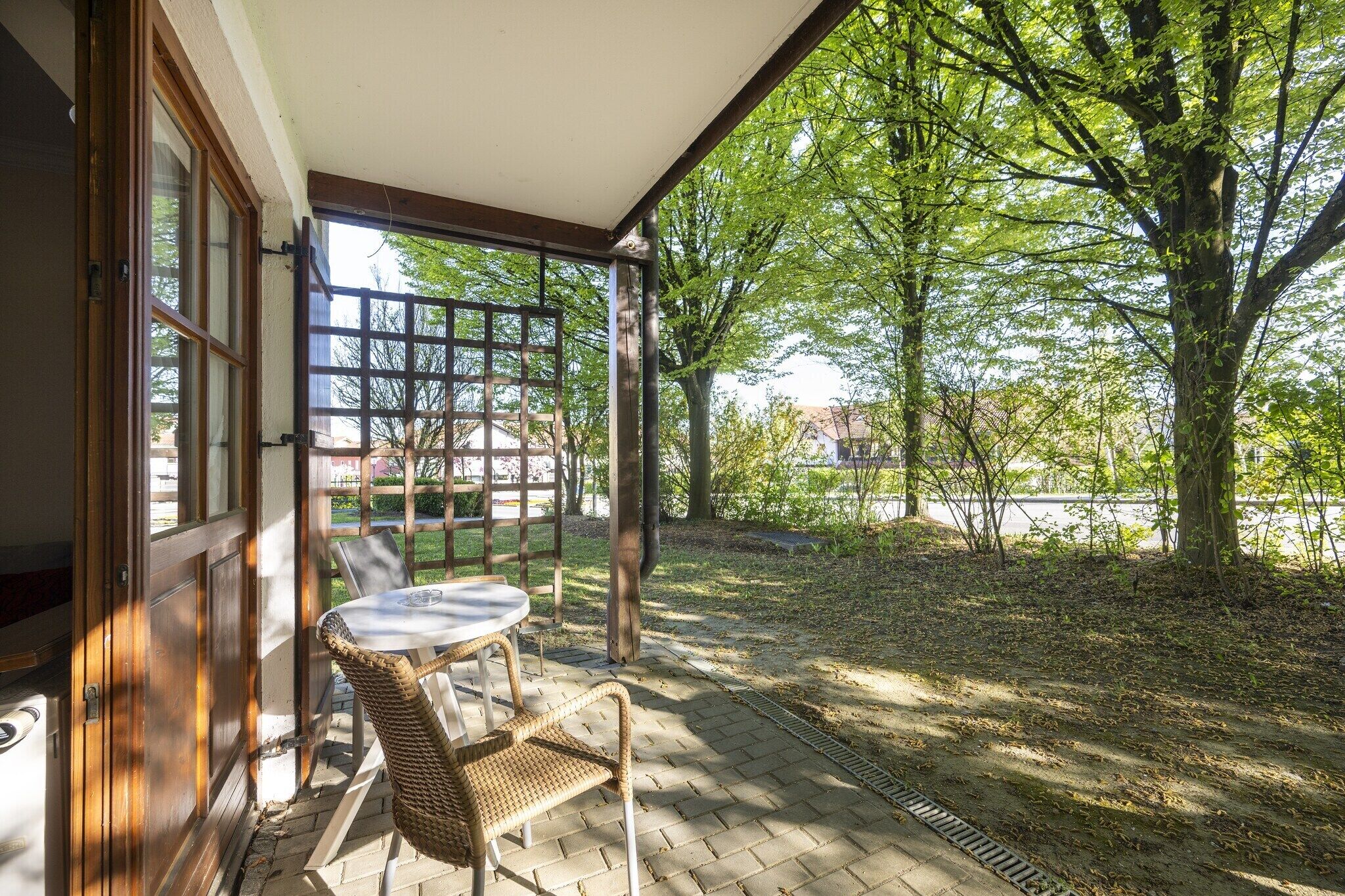 Une terrasse couverte avec une table et des chaises, une clôture en bois et un arbre en arrière-plan.