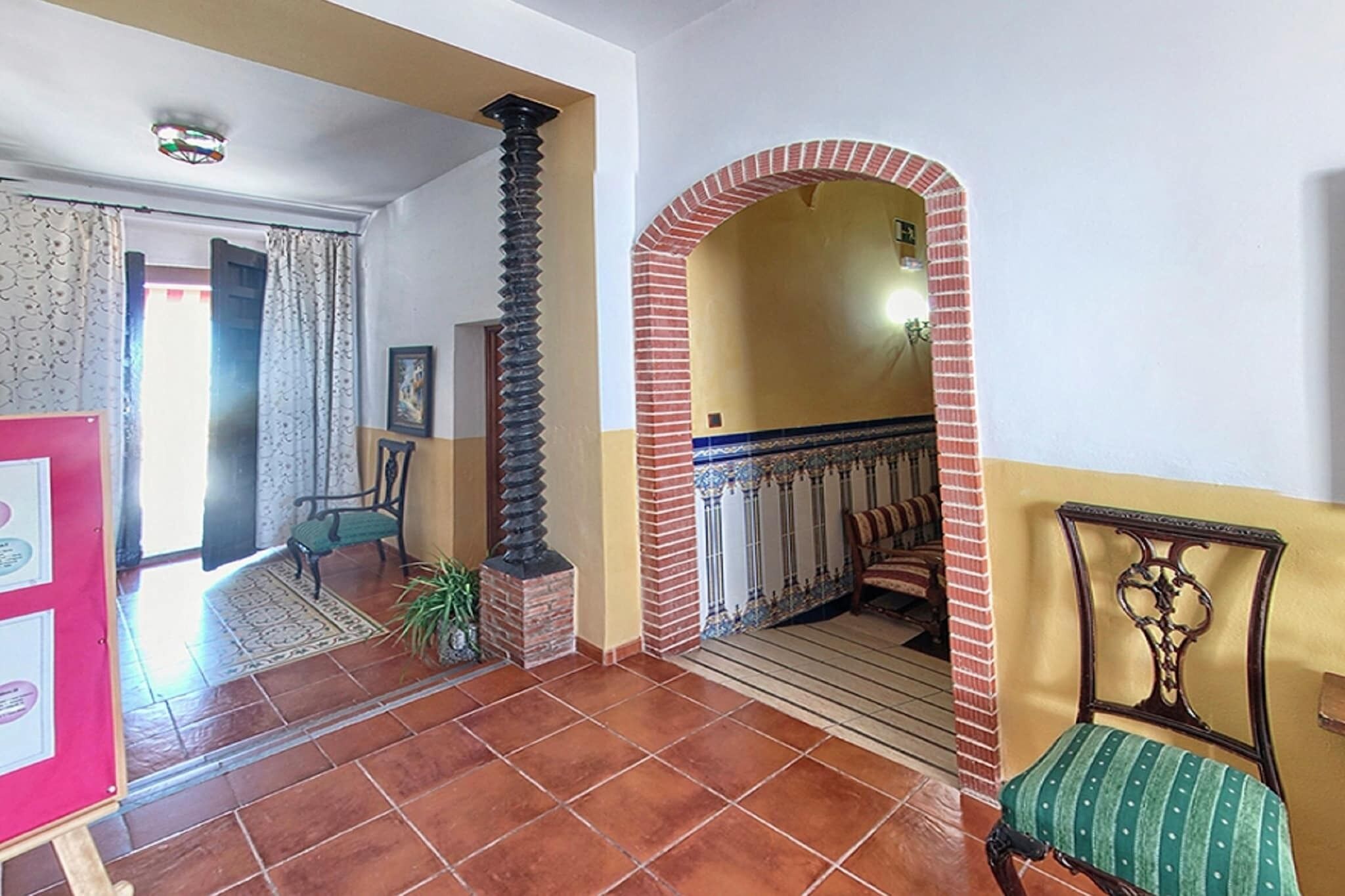 A spacious hallway with a tiled floor, a brick column, a bench, and a door leading to another room.